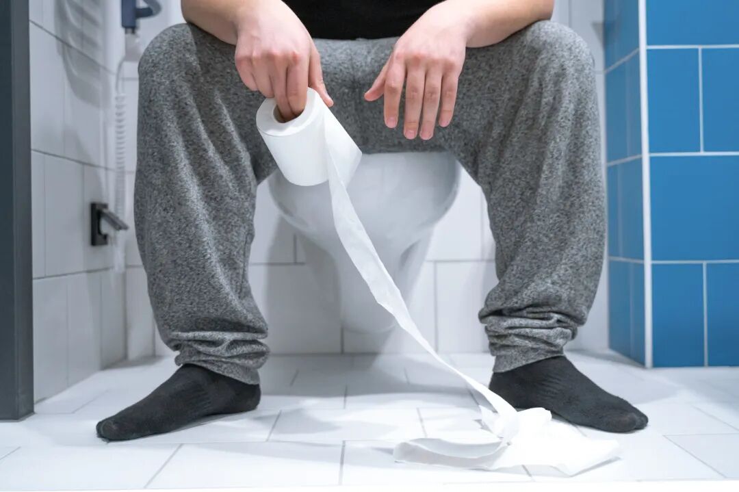 花瓣素材_男人坐在家里或酒店的白色马桶上，手里拿着卫生纸卷，把腿收起来。概念拍摄，室内，蓝白陶瓷墙壁和地板。_171183096.jpg